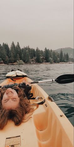 a woman laying on top of a yellow kayak in the middle of a body of water