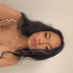 a woman with long black hair is posing for the camera while wearing gold jewelry and holding her hand up to her face