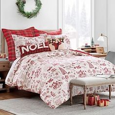 a christmas themed bedroom with red and white bedding, plaid pillowcases and wreath on the wall