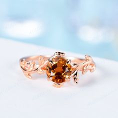 a close up of a ring with an orange stone in the center and leaves on it