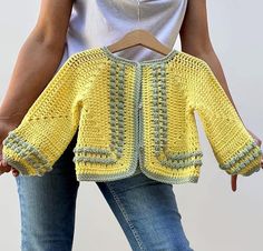 a crocheted sweater is being held up by a woman's hands,