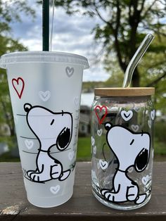 two tumblers sitting next to each other on top of a wooden table in front of trees