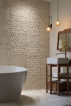 a white bath tub sitting next to a sink in a bathroom with stone wallpaper