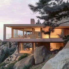 a house on top of a cliff with trees and rocks in the foreground at dusk