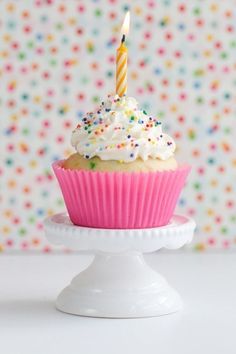 a cupcake with white frosting and a single lit candle on top is sitting on a cake plate