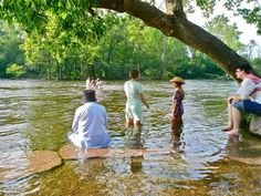 some people are sitting on rocks in the water and one person is standing up looking at something