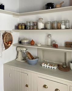 a kitchen with white cabinets and shelves filled with cooking utensils, bowls, and other items