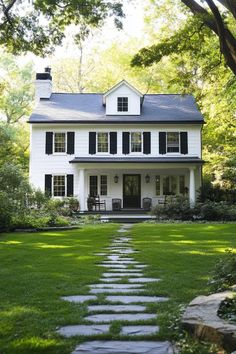 a white house with black shutters and stone walkway leading to the front door is surrounded by lush green grass