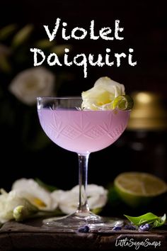 a close up of a drink in a glass on a table with flowers behind it