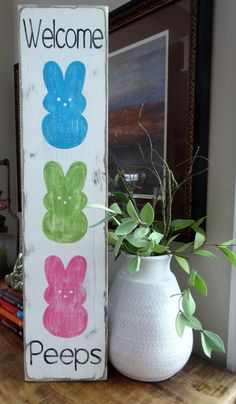 a welcome peeps sign sitting on top of a wooden table next to a potted plant