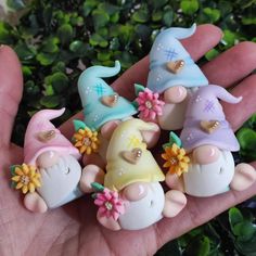 a hand is holding several small figurines in the shape of gnomes with flowers