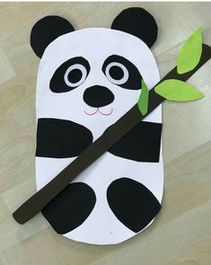 a paper panda bear holding a green leaf on top of a wooden floor with scissors