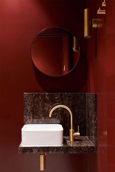 there is a sink and mirror in this bathroom with red walls, gold faucet, and marble countertop