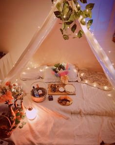 a bed topped with lots of food under a white tent covered in string lights and greenery