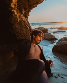 a man sitting on the beach next to some rocks