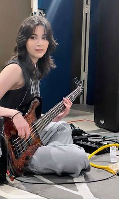 a woman sitting on the floor with a guitar in her hand and headphones around her neck