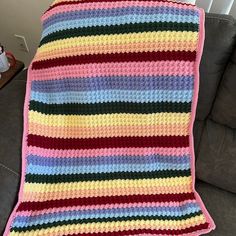 a multicolored crocheted blanket sitting on top of a couch next to a pillow