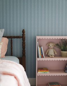 a teddy bear sitting on top of a book shelf next to a bed with pillows