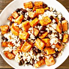 a white bowl filled with rice, beans and tofu on top of a wooden table