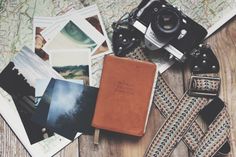 an old camera and some pictures on a wooden table next to a map with a leather cover