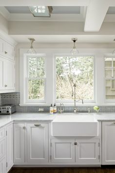 a kitchen with white cabinets and marble counter tops, along with two windows that look out onto the woods