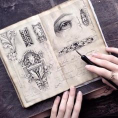 a person holding a pen and looking at an open book with drawings on it in front of them