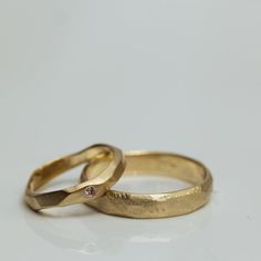 two gold wedding rings sitting side by side on a white surface with a diamond in the middle