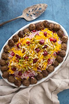 a white plate topped with meatballs covered in shredded cheese and other toppings next to a spoon