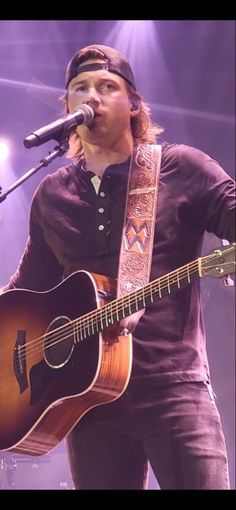 a man holding a guitar while standing in front of a microphone on top of a stage