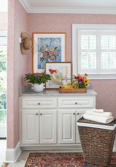 a bathroom with pink wallpaper and white cabinetry, flowers on the counter top