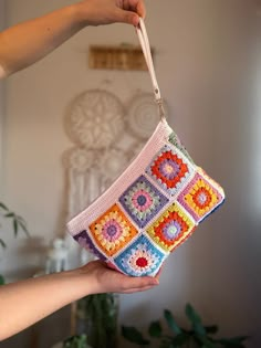 a hand holding a crocheted purse in front of a wall hanging planter