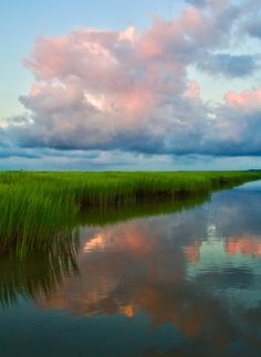 the clouds are reflected in the water and green grass is growing on both sides of the lake