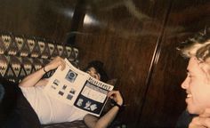 a man laying on top of a couch next to a woman holding up a newspaper