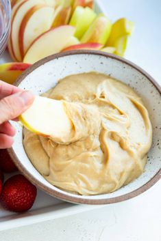 an apple being dipped with peanut butter in a bowl next to strawberries and apples