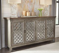 an ornate sideboard with two lamps on top and flowers in vases next to it