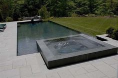 an outdoor swimming pool surrounded by grass and stone pavers, with water feature in the center