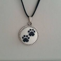 a cross stitch necklace with black and white dog paw prints