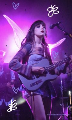 a woman holding a guitar while standing in front of a microphone