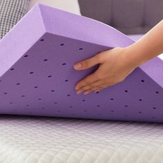 a person placing a purple object on top of a white bed with pillows in the background