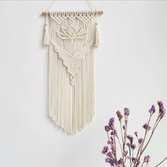 a white wall hanging next to a vase with purple flowers in it and a plant