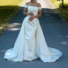 a woman in a white dress standing on the side of a road with her hands on her stomach