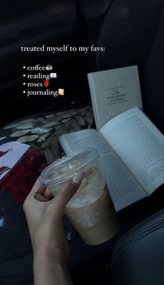 someone is reading a book and holding a cup of coffee while sitting in a car