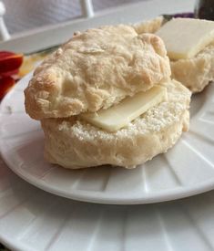 two biscuits with butter on top are sitting on a white plate next to a red flower