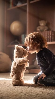 a little boy sitting on the floor kissing a teddy bear