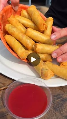 a plate with some food on it next to a bowl of sauce and a person's hand