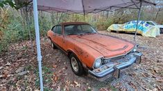 an old rusted car parked under a tent in the woods next to some trees