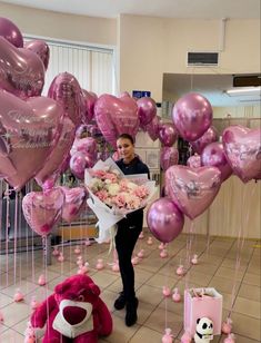 a woman holding a bouquet of flowers in front of balloons and stuffed animals on the floor