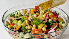 a person pouring dressing over a salad in a glass bowl on a white table top