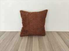 a brown pillow sitting on top of a wooden floor next to a white wall and wood floor