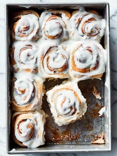 a baking pan filled with cinnamon rolls covered in icing on top of a marble counter